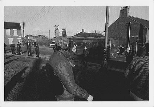 Greetings card of pickets gestitulacing to working miners in a coach on Station Road, Easington Colliery, County Durham, during February 1985.